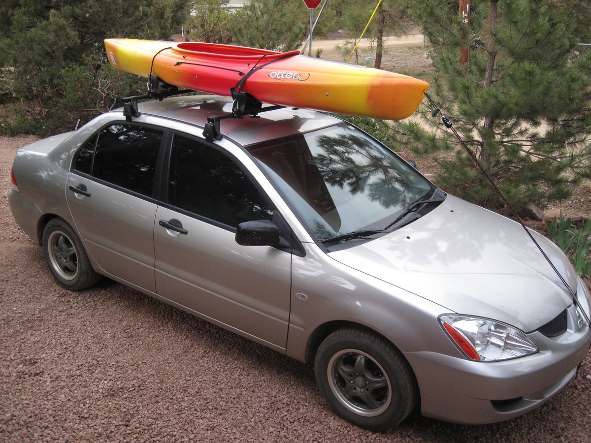 A kayak strapped to a car roof rack with cam straps